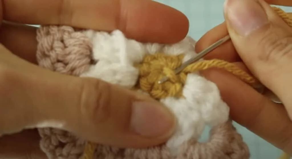 Using a sewing needle to weave yarn tails in on a finished daisy granny square tutorial
